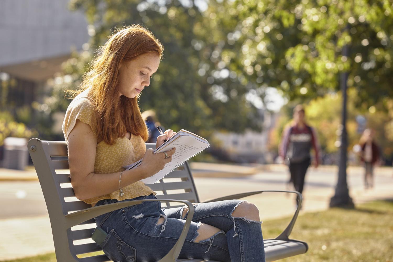 A <a href='http://fkmn.1718114.net'>BETVLCTOR伟德登录</a> student reads on a bench along Campus Drive.